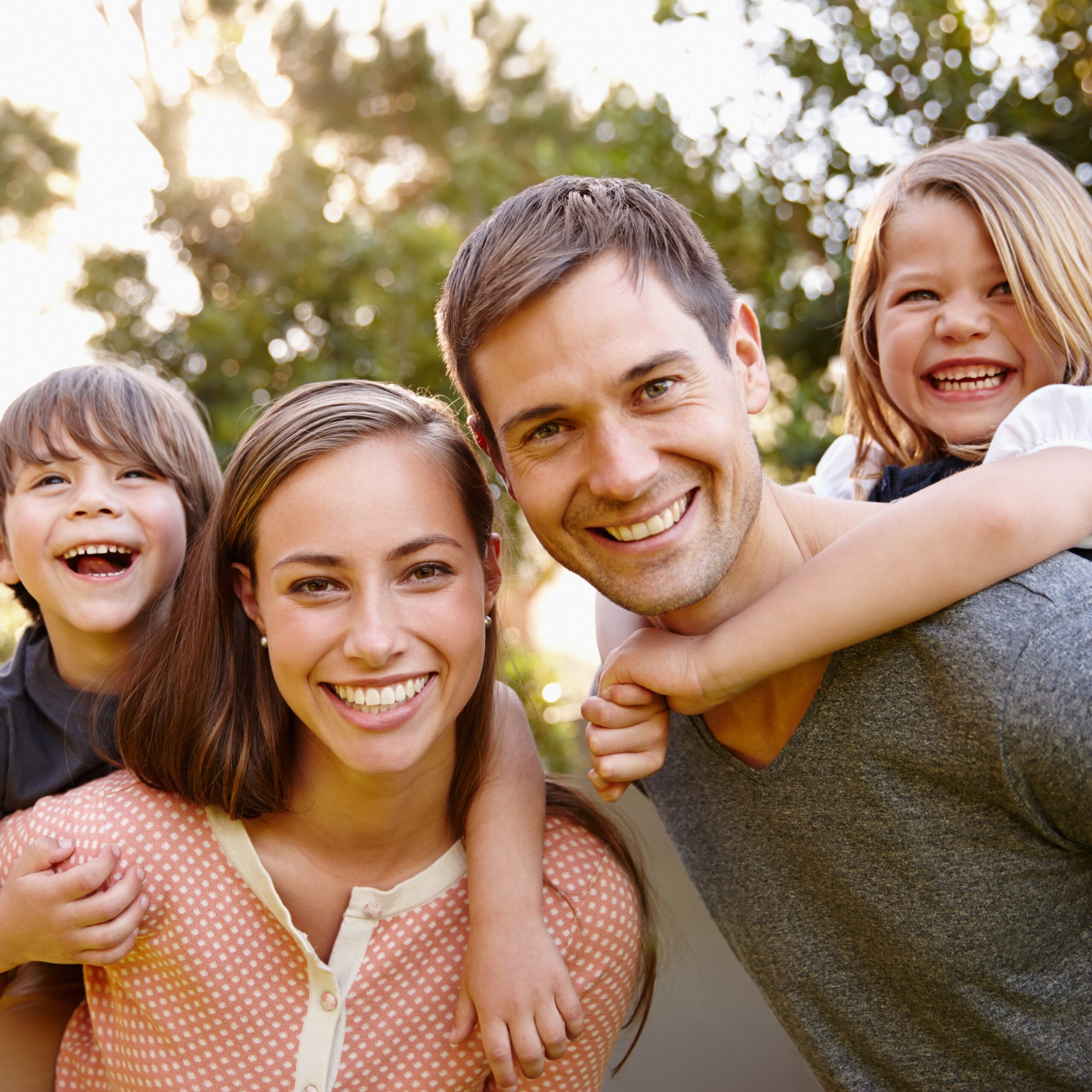 A portrait of a happy young couple giving their children piggyback rides outside